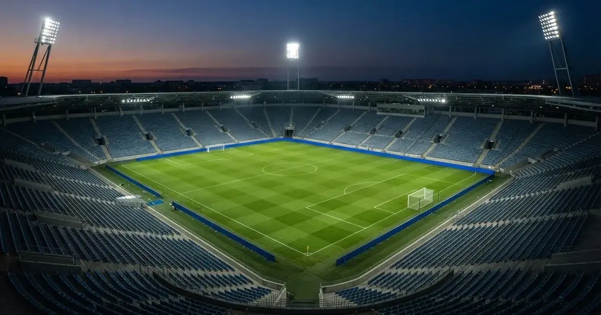 Szeroki widok na pusty stadion piłkarski z wysokiego narożnika, reflektory jarzą się w błękitnej godzinie.